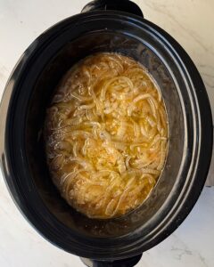overhead shot of cooked chicken and onions in a black slow cooker
