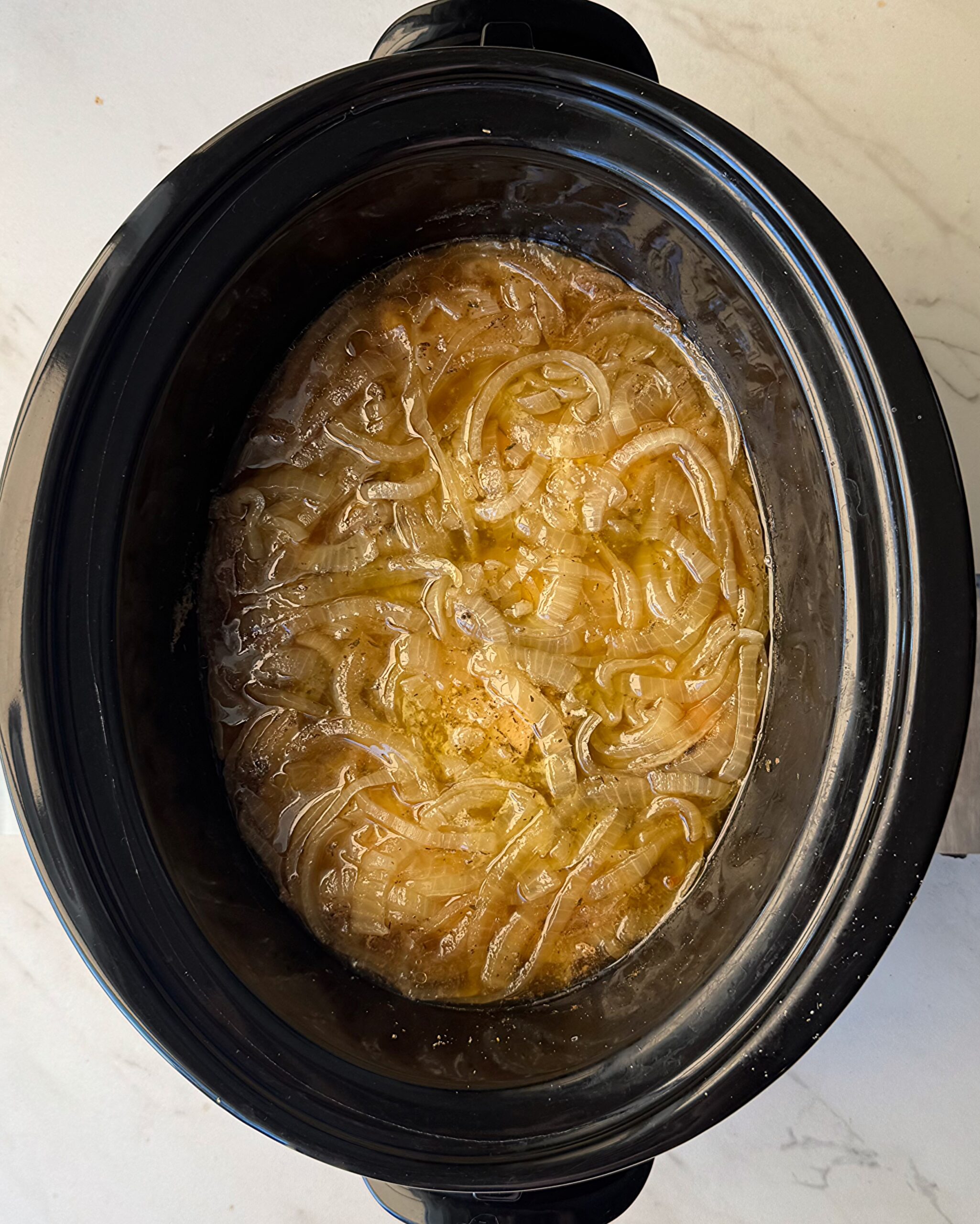 overhead shot of cooked chicken and onions in a black slow cooker