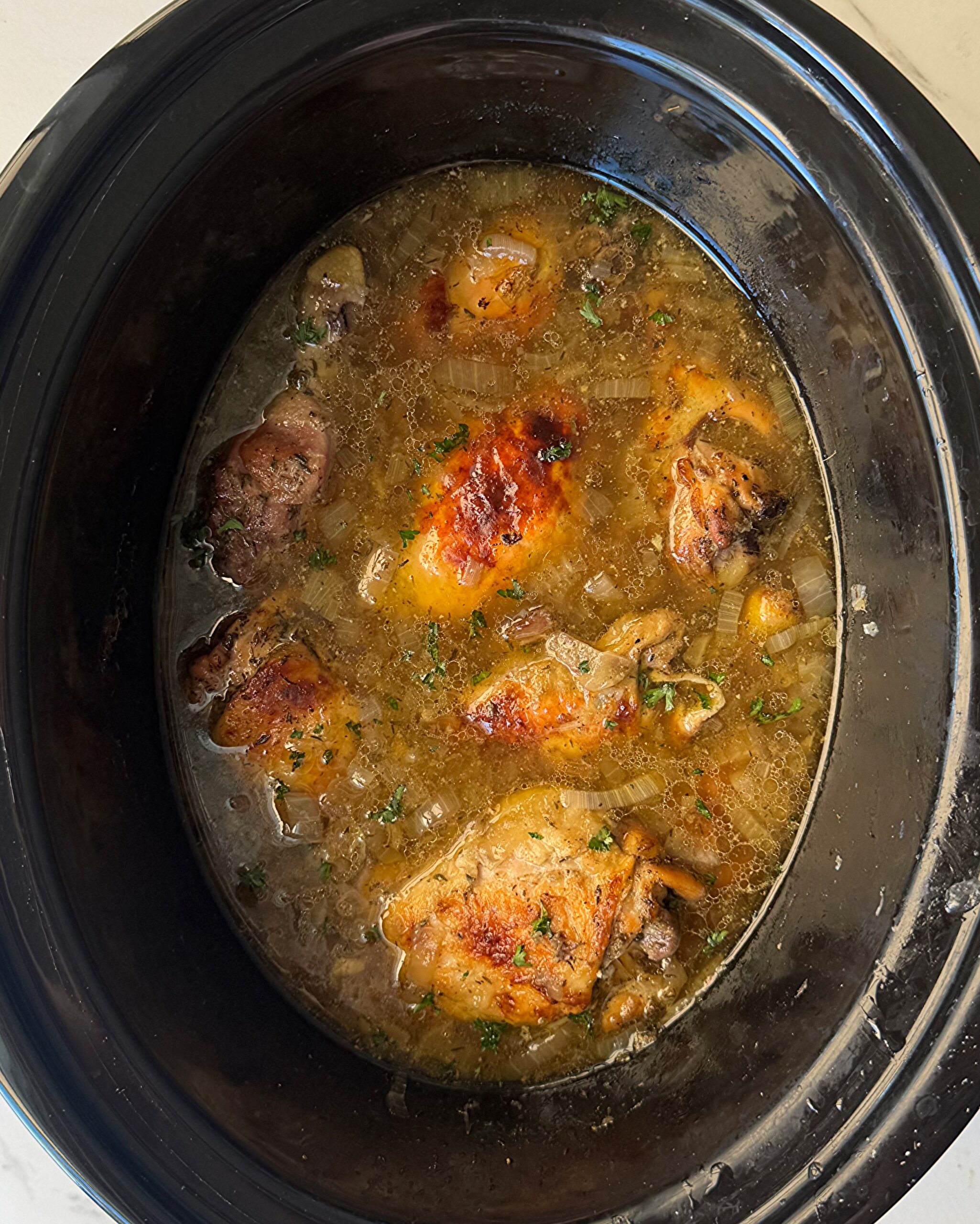 overhead shot of cooked chicken and onions garnished with fresh parsley in a black slow cooker