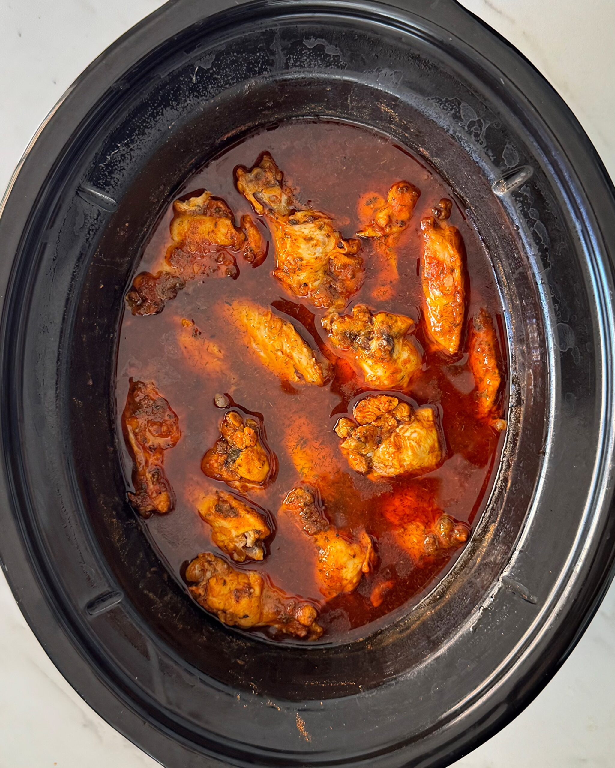 overhead shot of cooked Buffalo wings in a black slow cooker