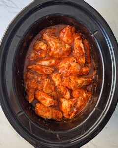 overhead shot of uncooked Buffalo wings in a black slow cooker