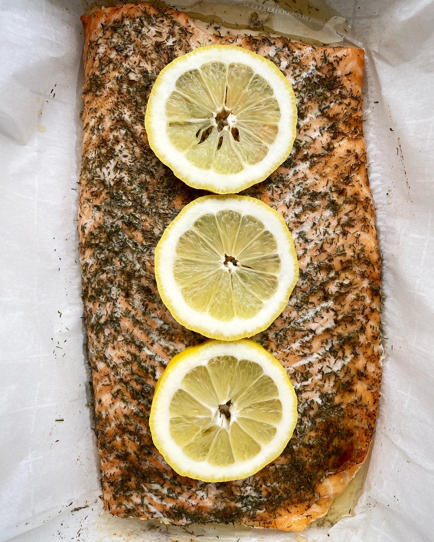 overhead shot of cooked, seasoned salmon in a white slow cooker on top of parchment paper