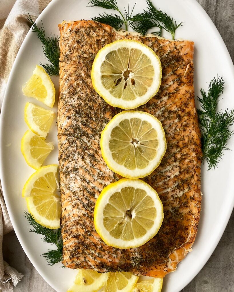 overhead shot of cooked lemon dill salmon topped with lemon slices & garnished with fresh dill on white plate