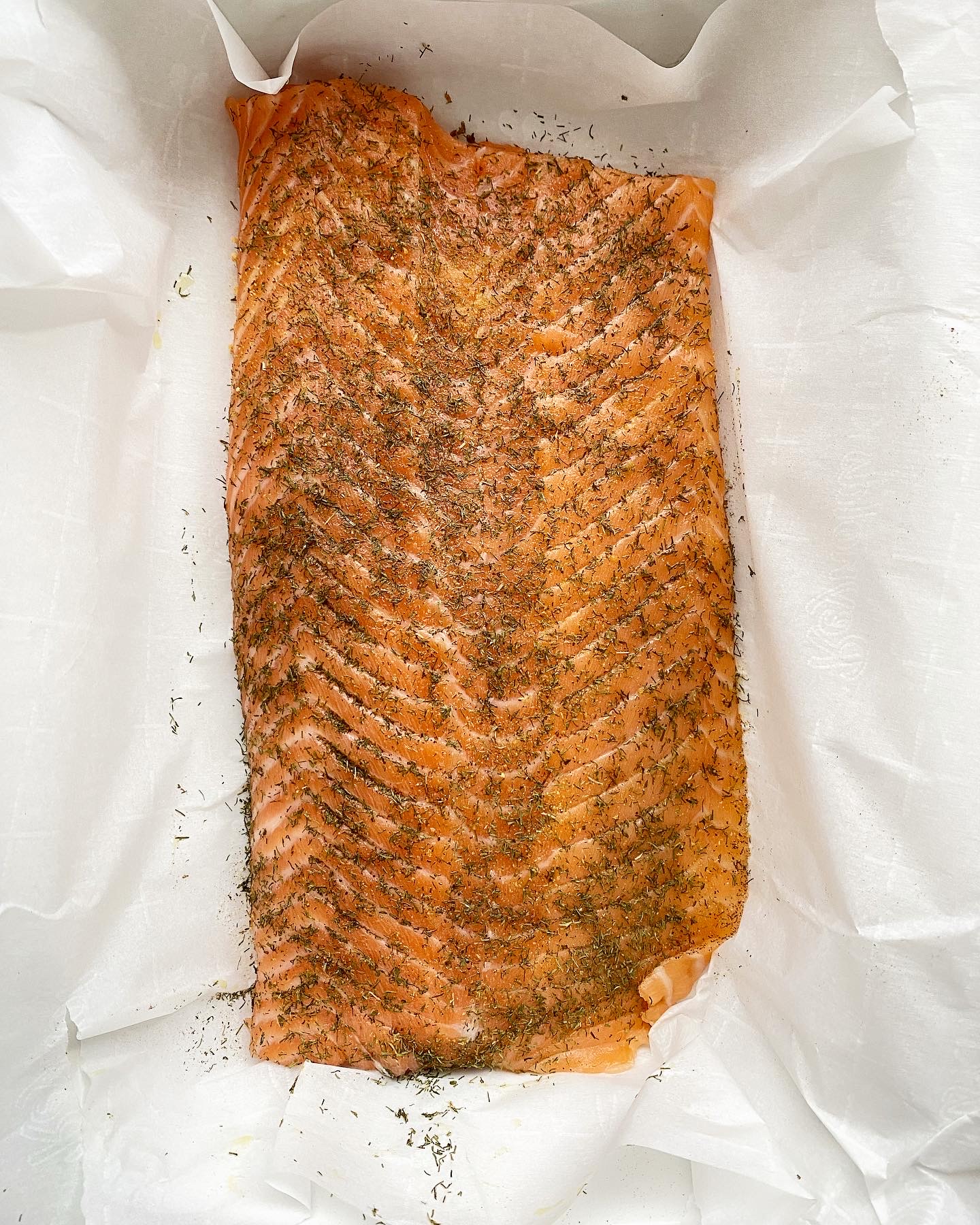 overhead shot of uncooked, seasoned salmon in a white slow cooker on top of parchment paper