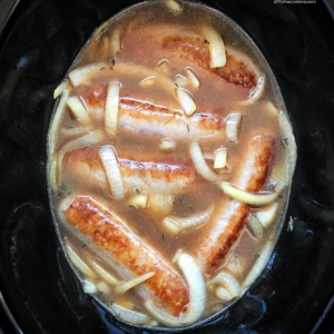 overhead shot of uncooked bangers and mash in a black slow cooker