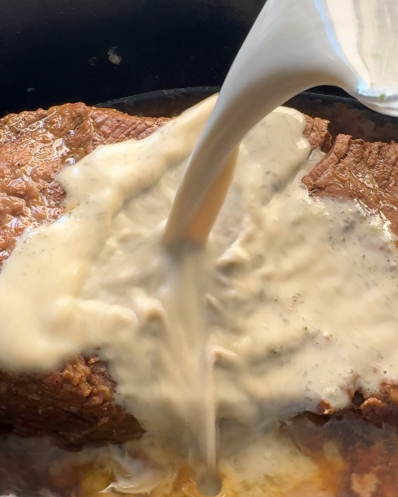 close up shot of pouring horseradish sauce on top olf cooked brisket.
