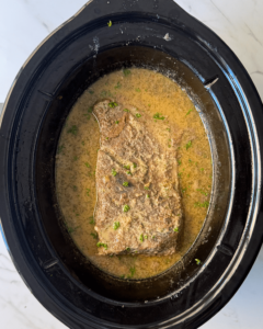 overhead shot of cooked horseradish brisket in a black slow cooker