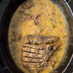 overhead shot of sliced, cooked horseradish brisket in a black slow cooker