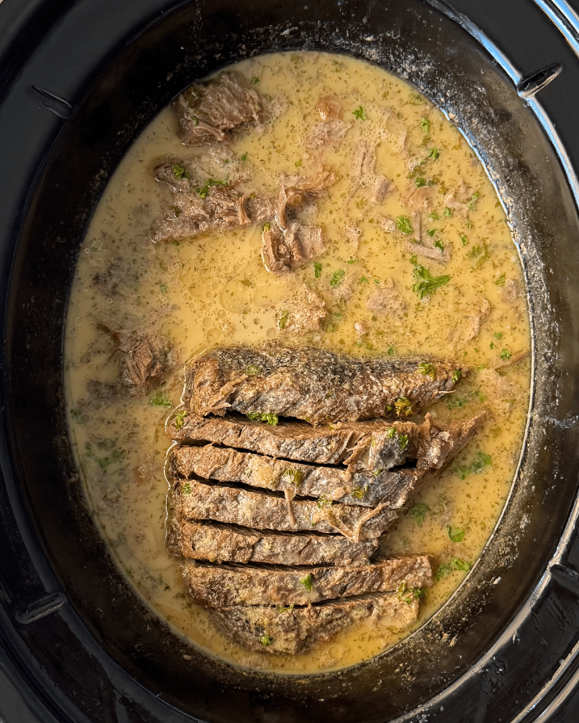 overhead shot of sliced, cooked horseradish brisket in a black slow cooker