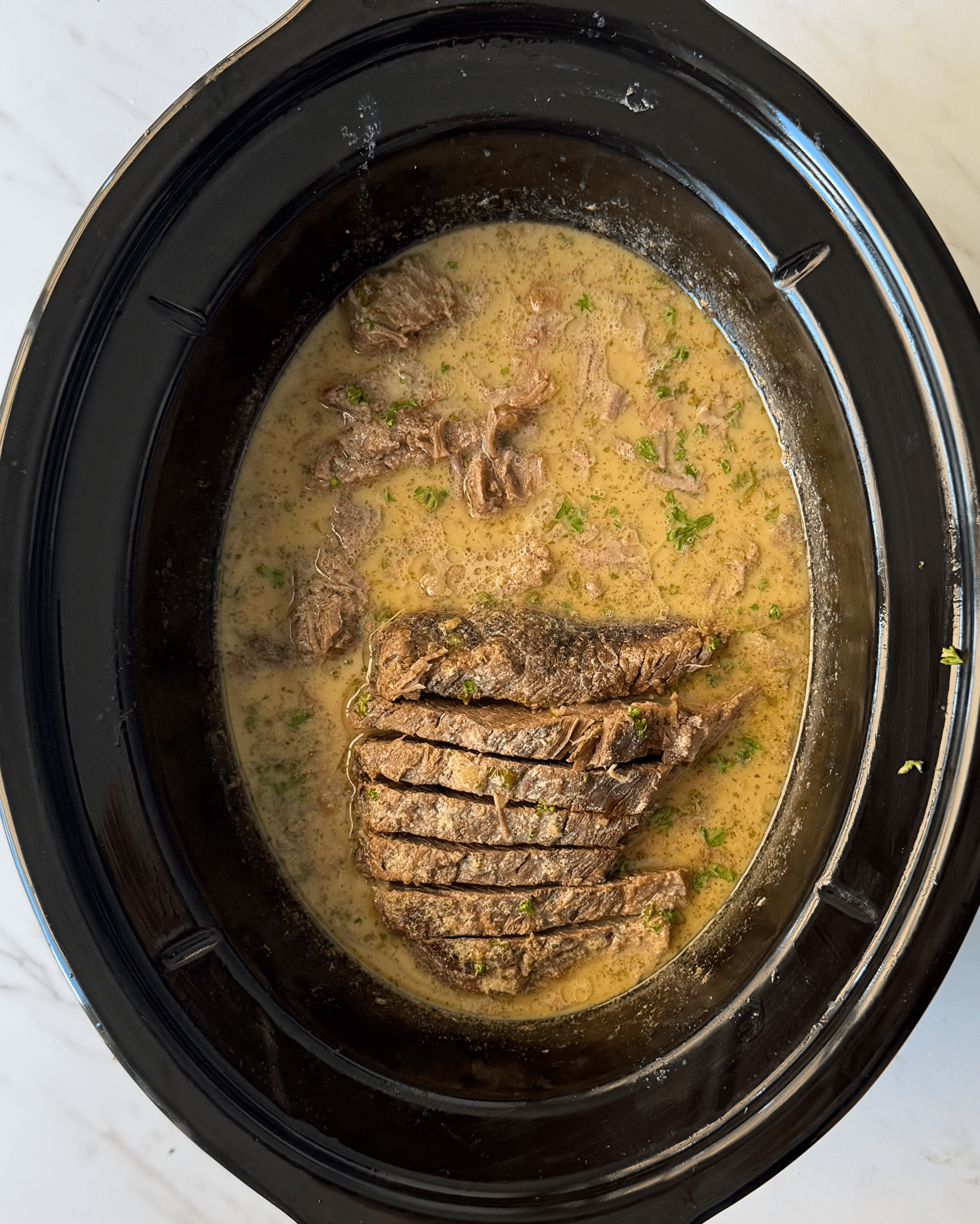 overhead shot of sliced, cooked horseradish brisket in a black slow cooker