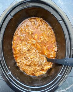 overhead shot of cooked, shredded pulled pork in a black slow cooker