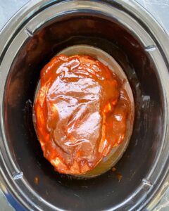 overhead shot of uncooked, shredded pulled pork in a black slow cooker