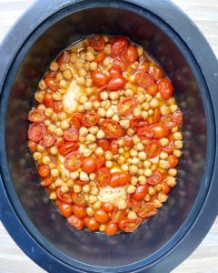 overhead shot of cooked crockpot chicken chickpeas tomatoes in a black slow cooker