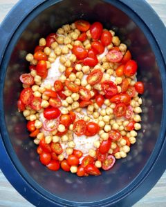 overhead shot of uncooked crockpot chicken chickpeas tomatoes in a black slow cooker