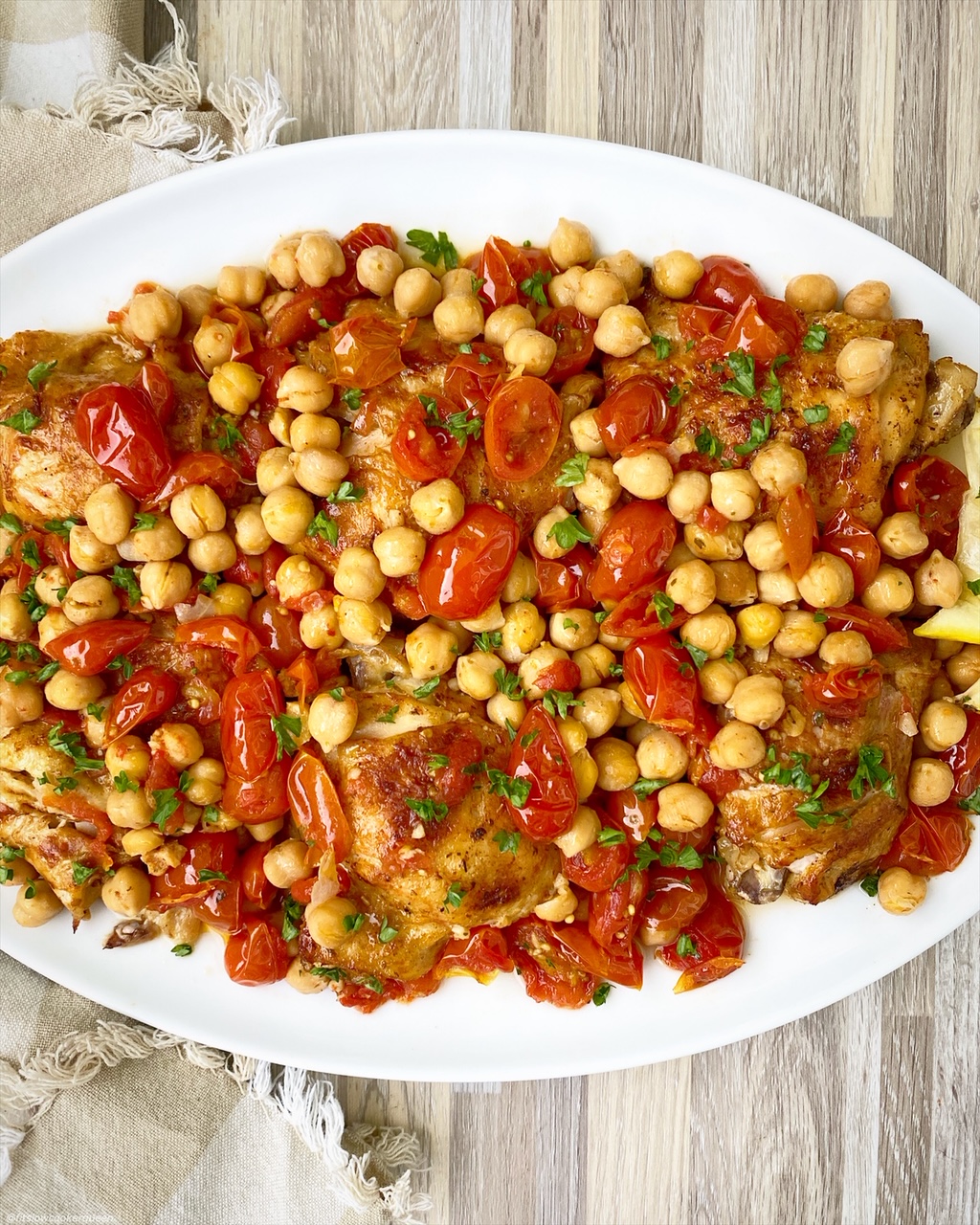 cooked chicken, chickepeas and tomatoes on a white serving platter