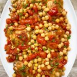 overhead shot of cooked crockpot chicken chickpeas tomatoes on a white plate garnished with fresh parsley