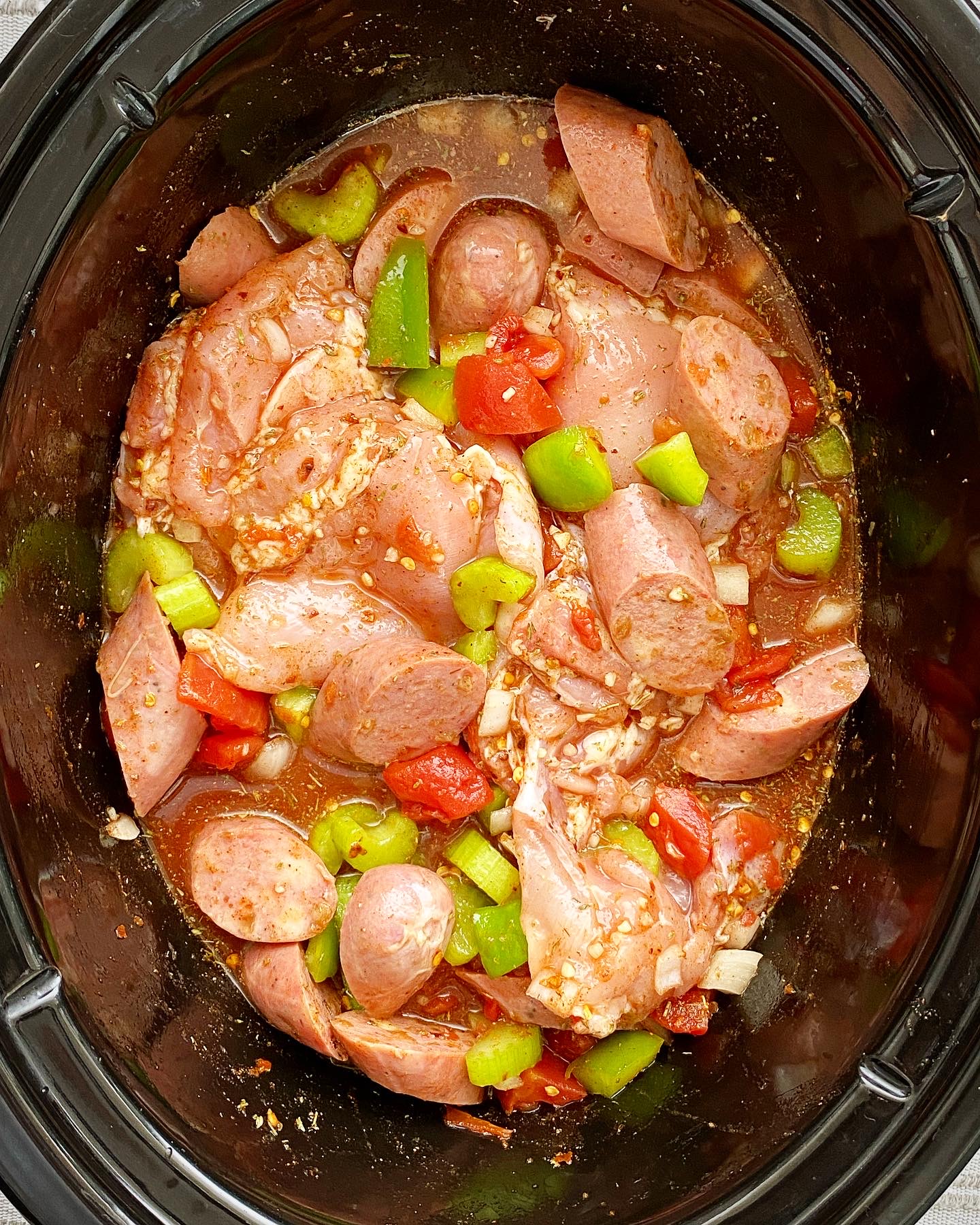 overhead shot of uncooked spicy chicken sausage in a black slow cooker