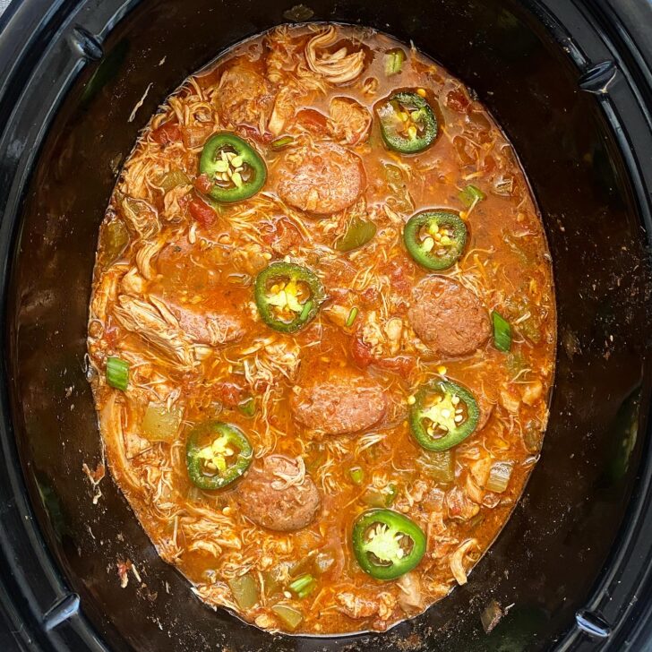 overhead shot of cooked spicy chicken sausage in a black slow cooker garnished with slices of jalapeno