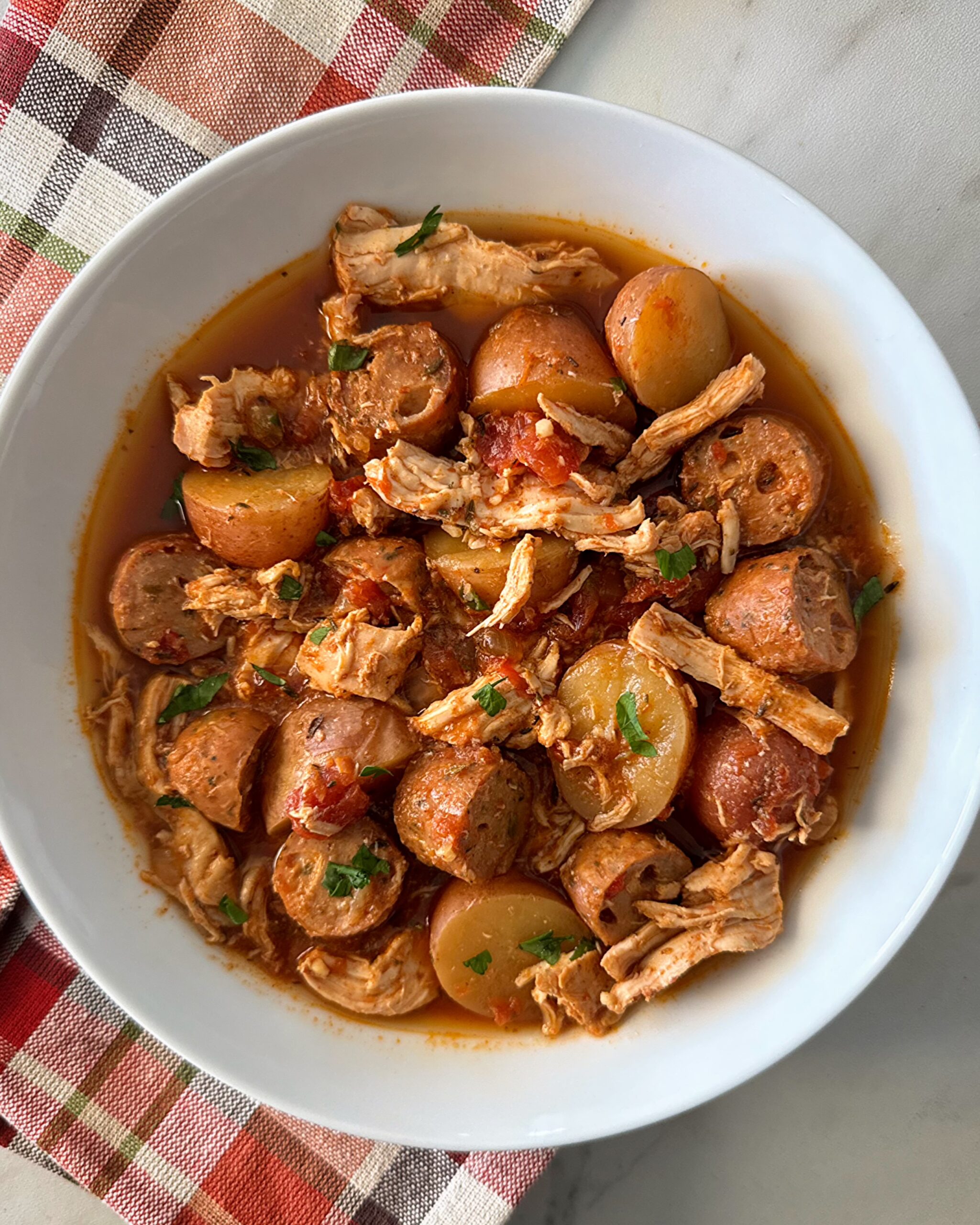 overhead shot of cooked spicy chicken and sausage in a white bowl garnished with fresh parsley