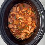 overhead shot of cooked spicy chicken and sausage in a black slow cooker garnished with fresh parsley