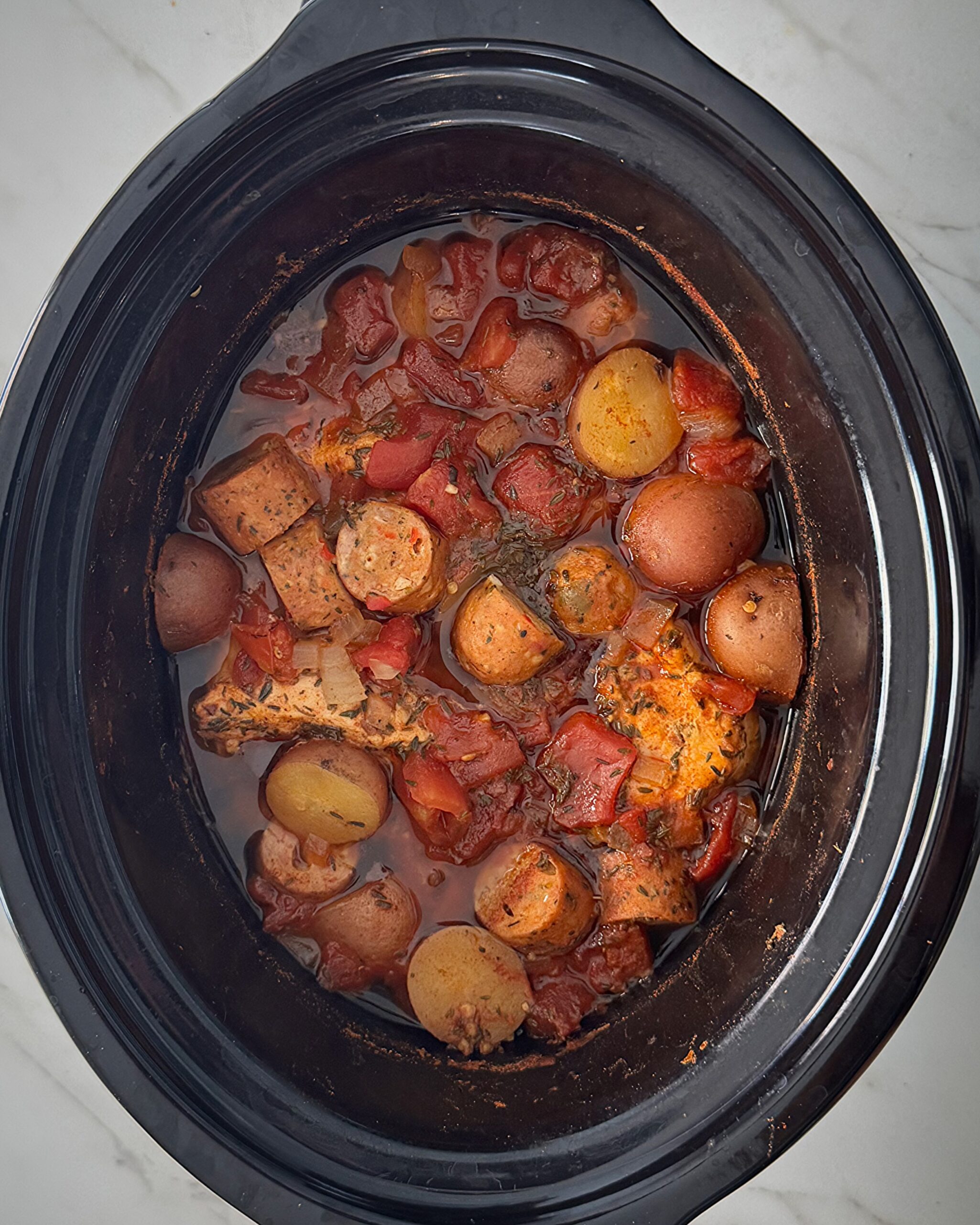 overhead shot of cooked spicy chicken and sausage in a black slow cooker