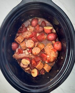 overhead shot of uncooked spicy chicken and sausage in a black slow cooker