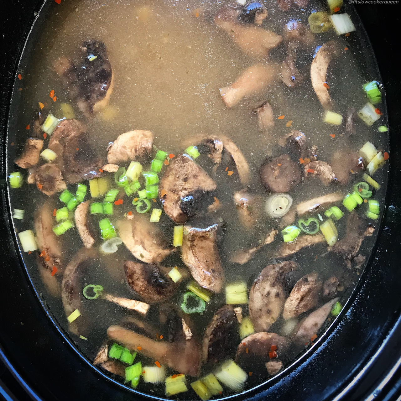 overhead shot of cooked tofu mushroom soup in a black slow cooker