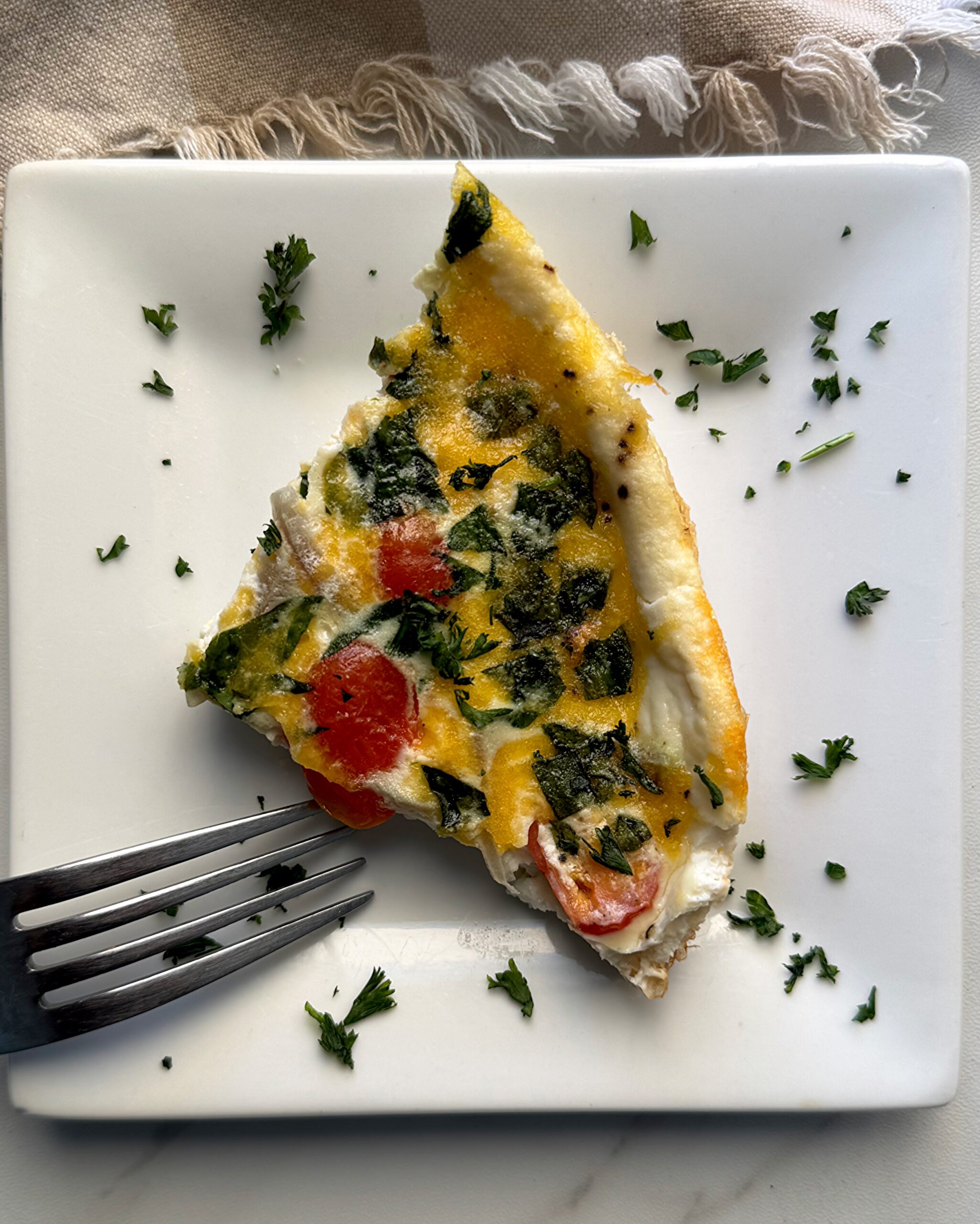 overhead shot of a slice of Slow Cooker Egg White Fritatta on a white plate garnished with fresh parsley