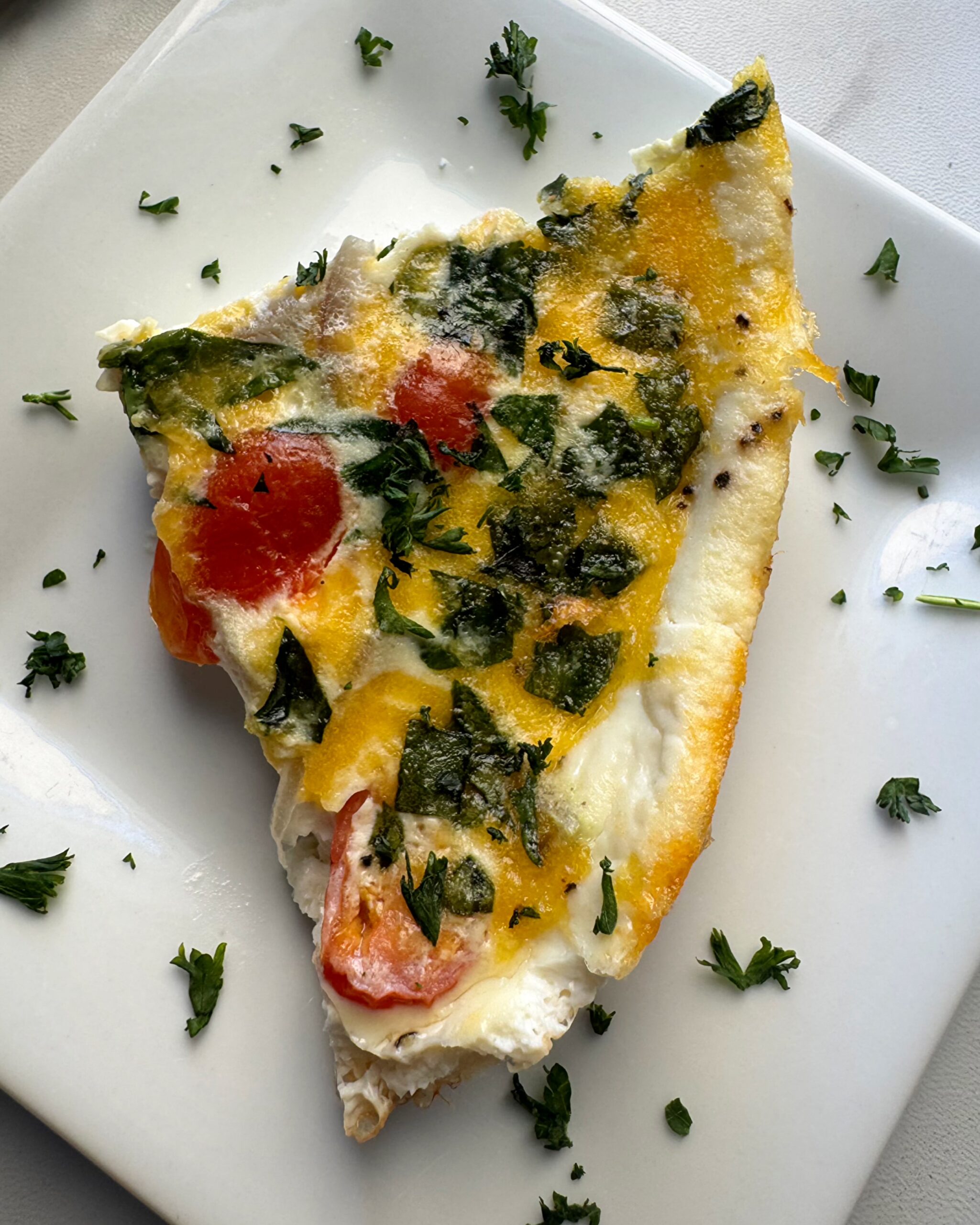 close up shot of a slice of Slow Cooker Egg White Fritatta on a white plate garnished with fresh parsley