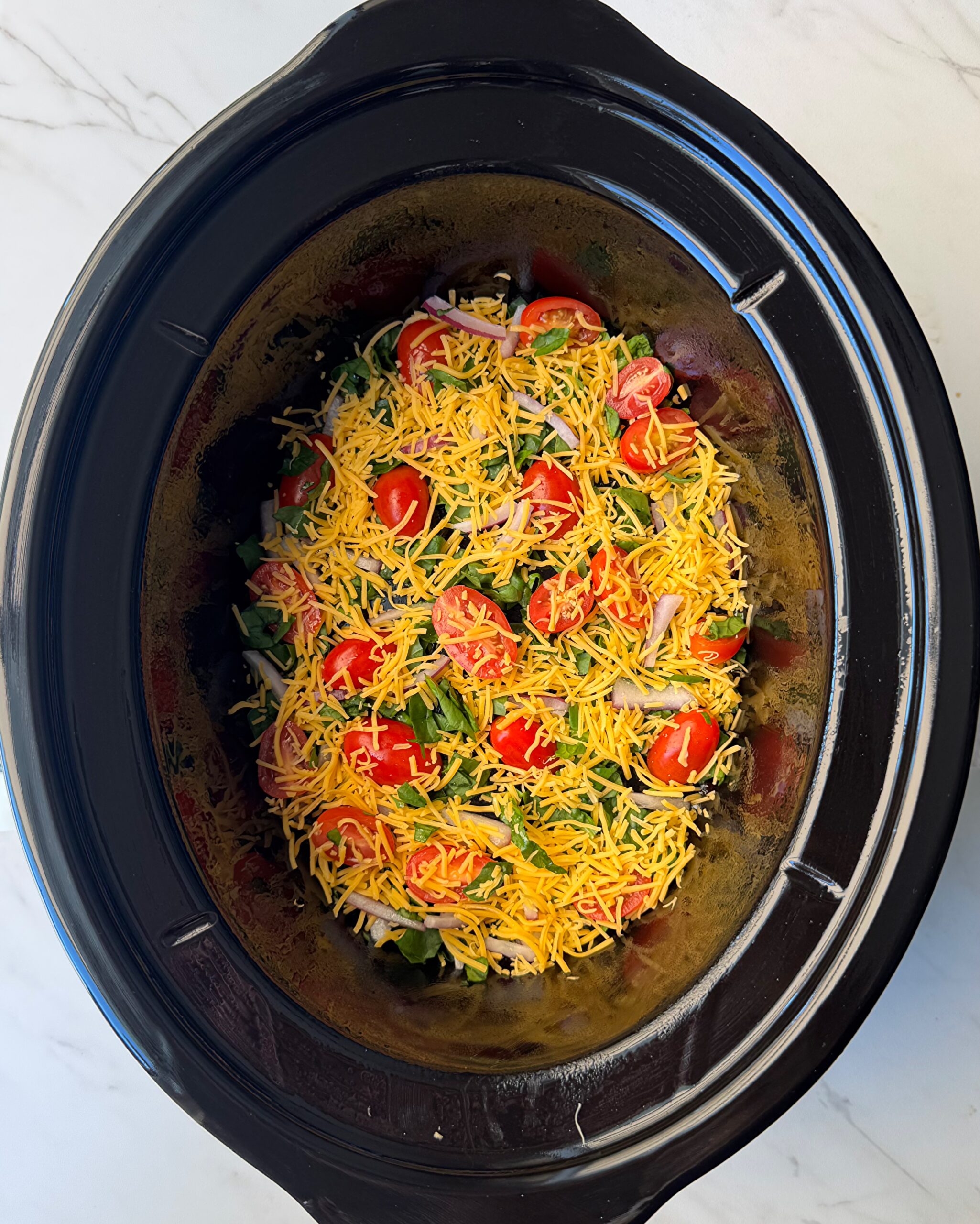 overhead shot of vegetables and cheese in a black slow cooker
