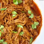 close up shot of shredded enchilada in a white bowl garnished with cilantro