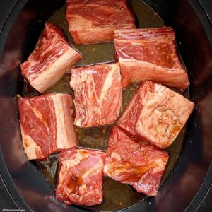 overhead shot of uncooked short ribs in a black slow cooker