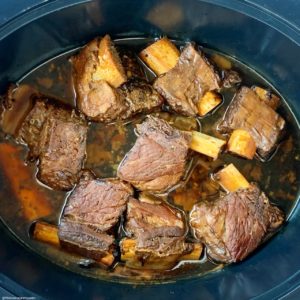 overhead shot of cooked short ribs in a black slow cooker