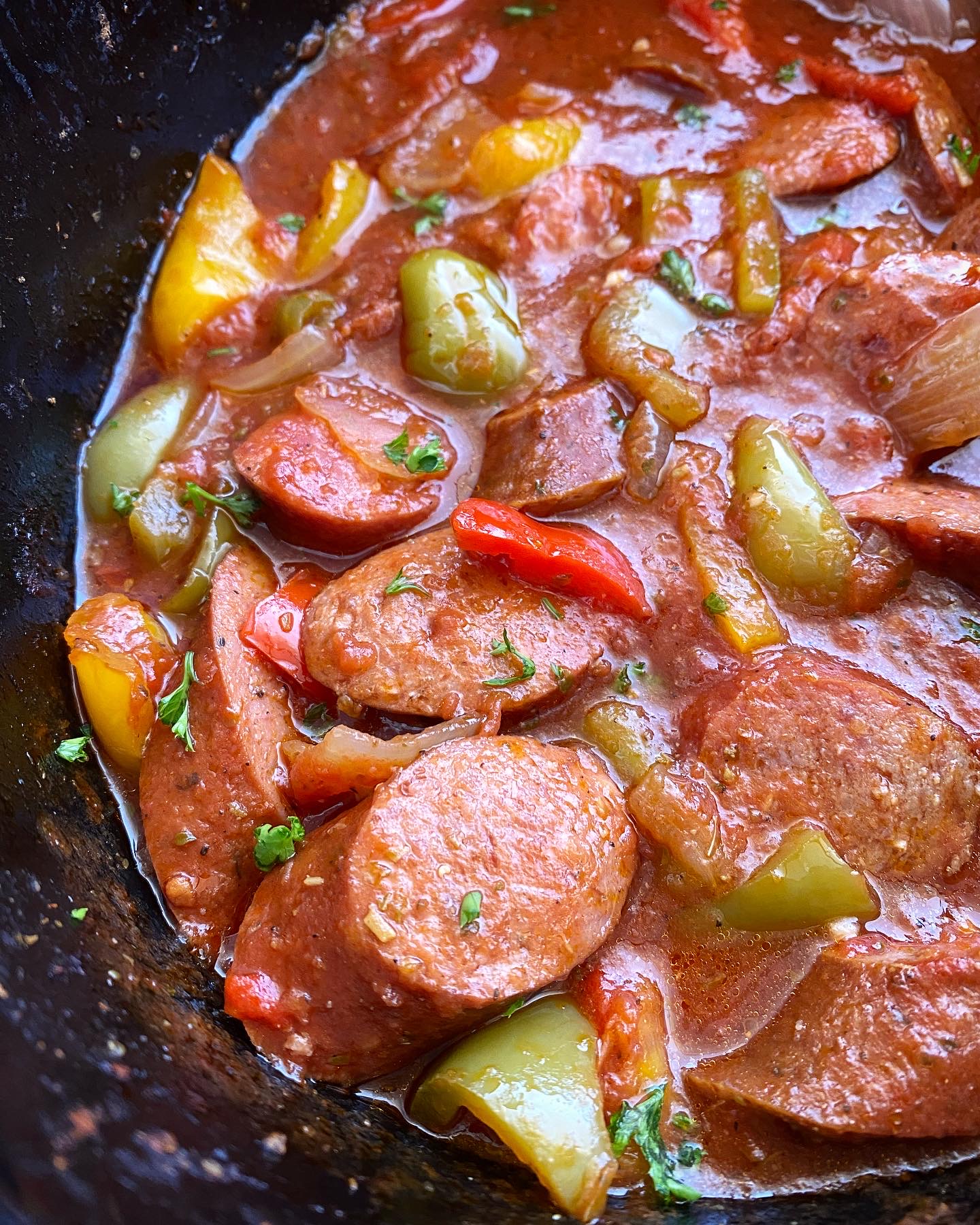 close up shot of cooked sausage, bell pepper & onions in a black slow cooker