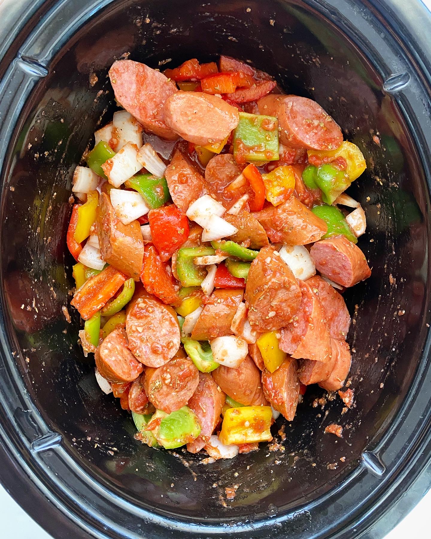 overhead shot of uncooked sausage, bell pepper & onions in a black slow cooker