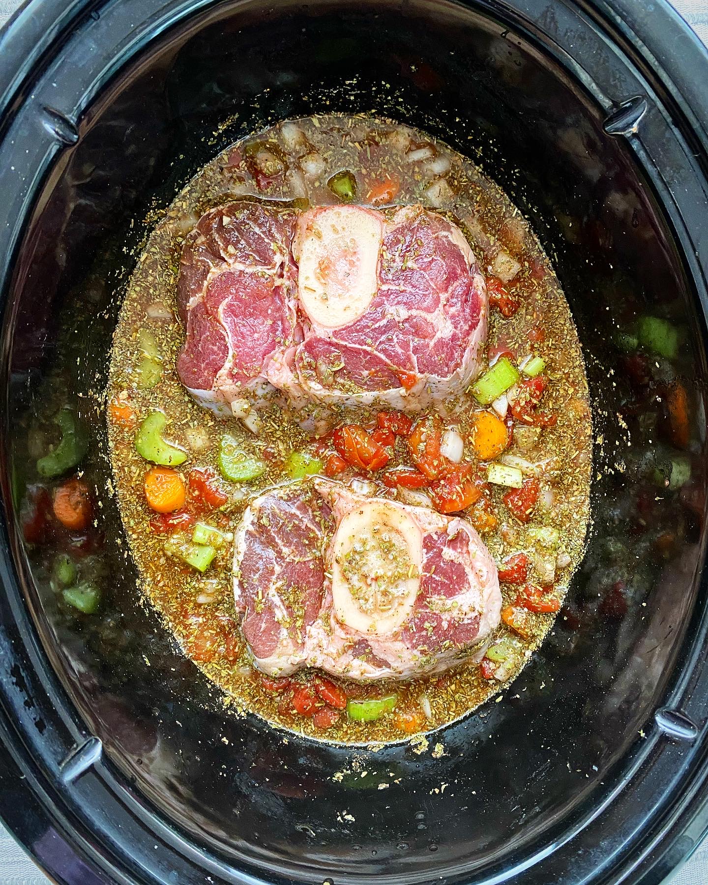 overhead shot of uncooked crockpot beef osso buco in a black slow cooker
