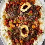 overhead shot of cooked crockpot beef osso buco on a white plate with mashed potatoes garnished with fresh parsley
