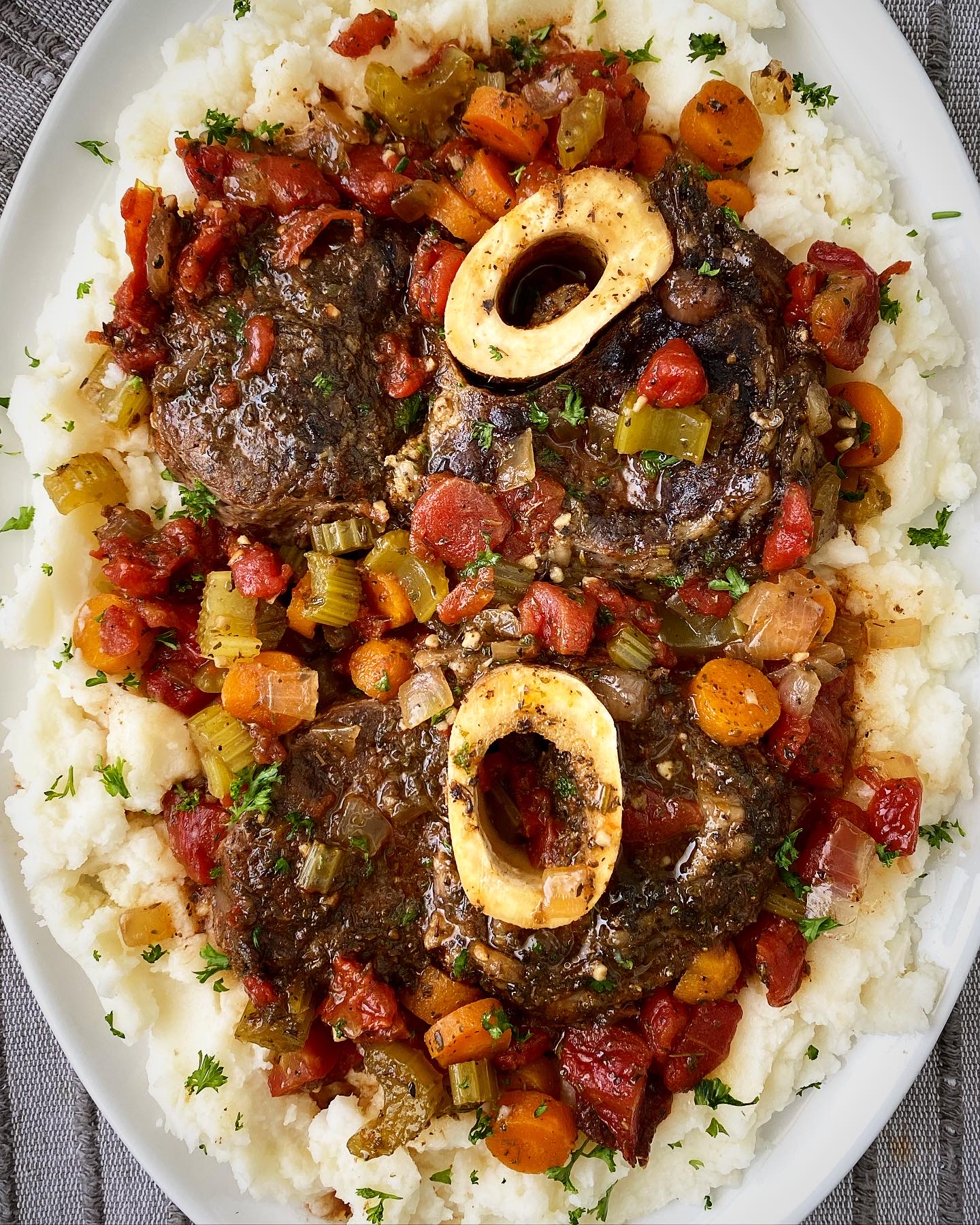 overhead shot of cooked crockpot beef osso buco on a white plate with mashed potatoes garnished with fresh parsley