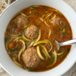 overhead shot of slow cooker meatball zoodle soup in a white bowl with a silver spoon