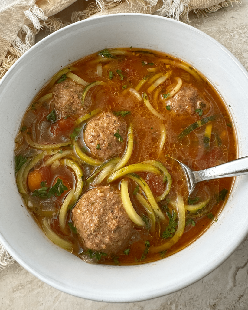 overhead shot of slow cooker meatball zoodle soup in a white bowl with a silver spoon