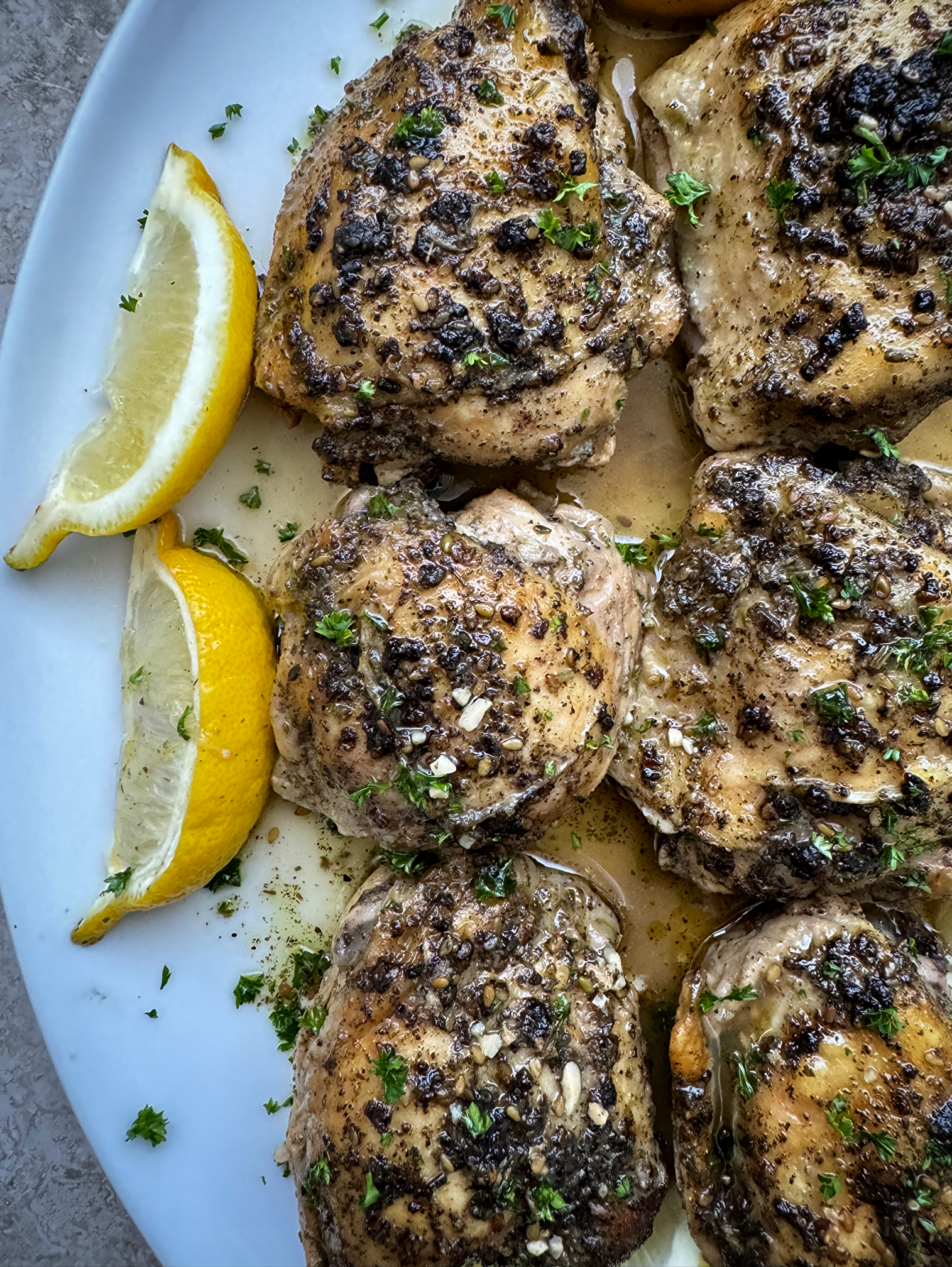 overhead shot of cooked zaatar chicken on a white plate garnished with lemon slices