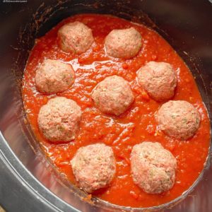 overhead shot of uncooked mozzarella stuffed meatballs in a tomato sauce in a black slow cooker