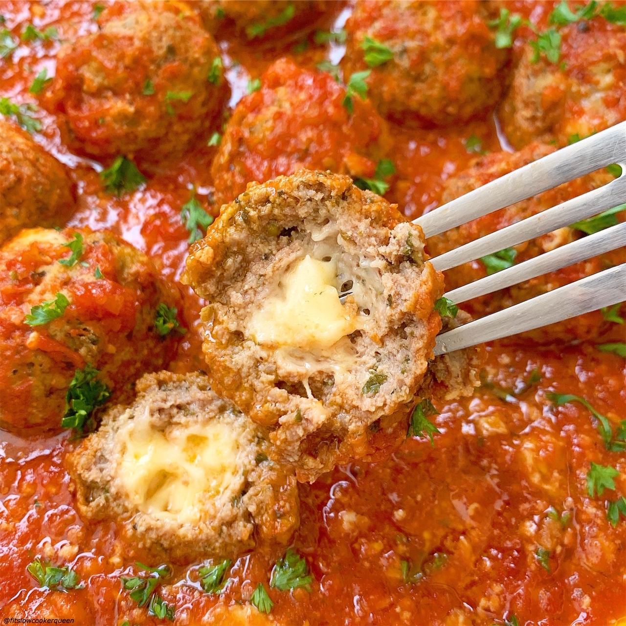 overhead shot of a sliced meatball on a fork with mozzarella oozing out