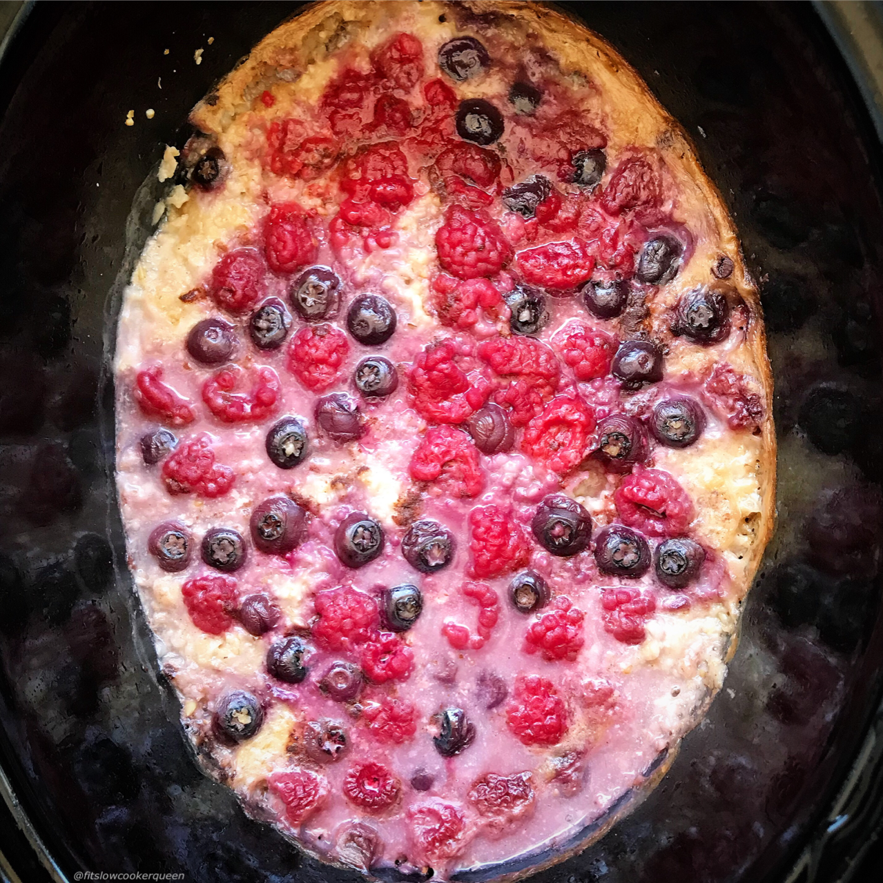 overhead shot of cooked berry oatmeal in a black slow cooker with the ingredients unstirred