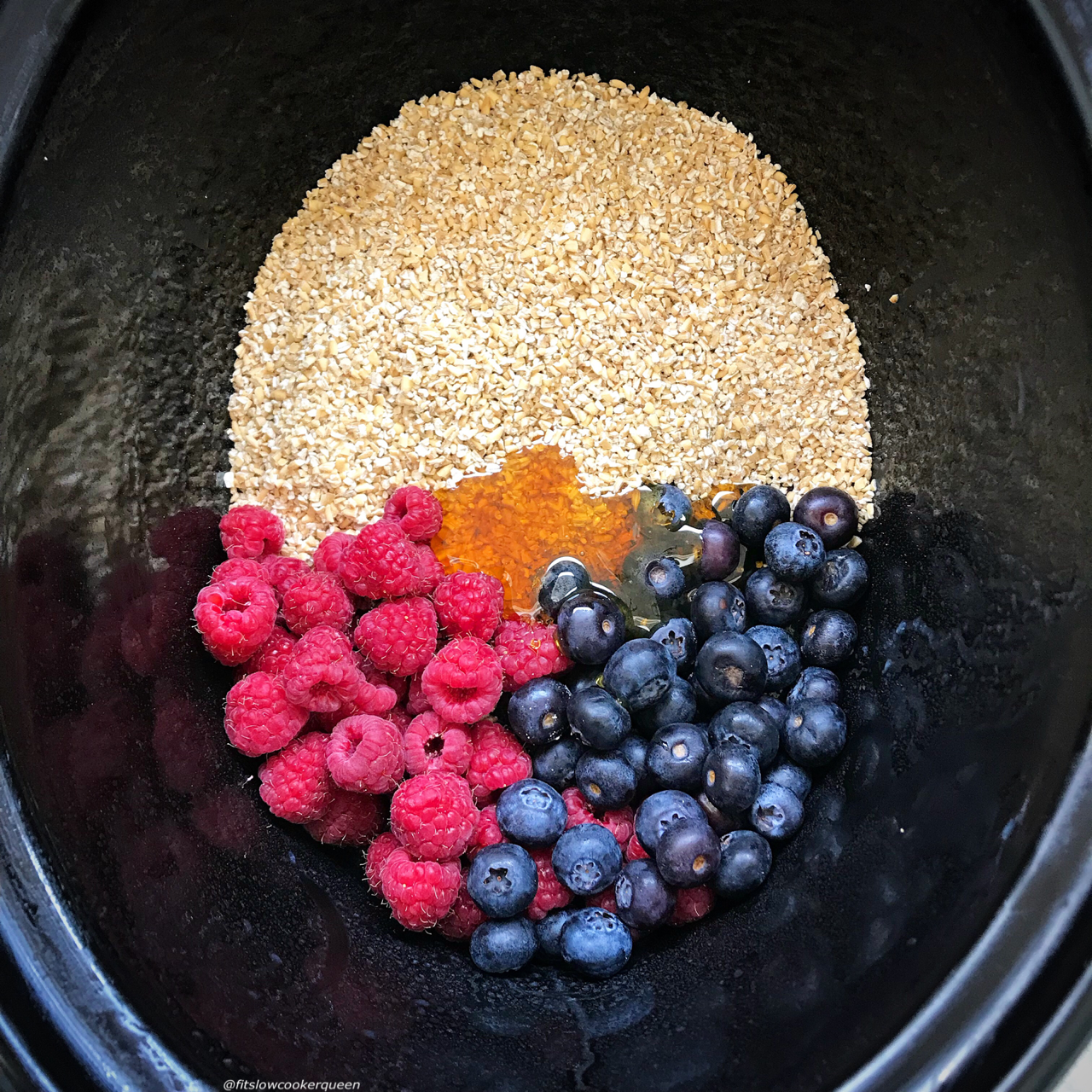 overhead shot of uncooked berry oatmeal in a black slow cooker with the ingredients unstirred