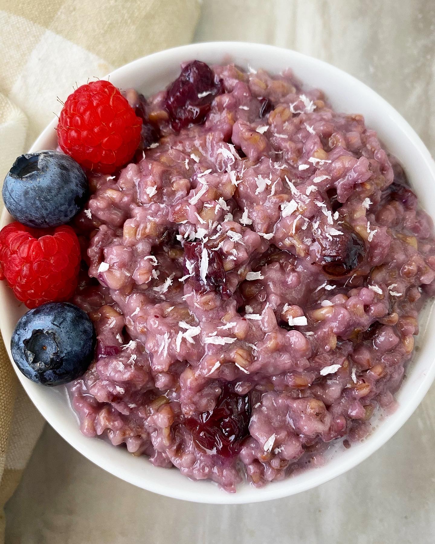 overhead shot of berry oatmeal in white bowl garnished with fresh berries & shredded coconut