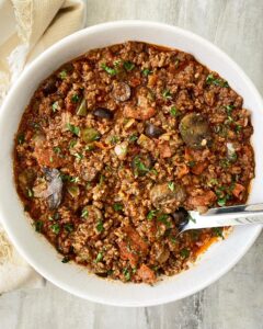 overhead shot of supreme pizza stew with a large silver spoon in a white bowl