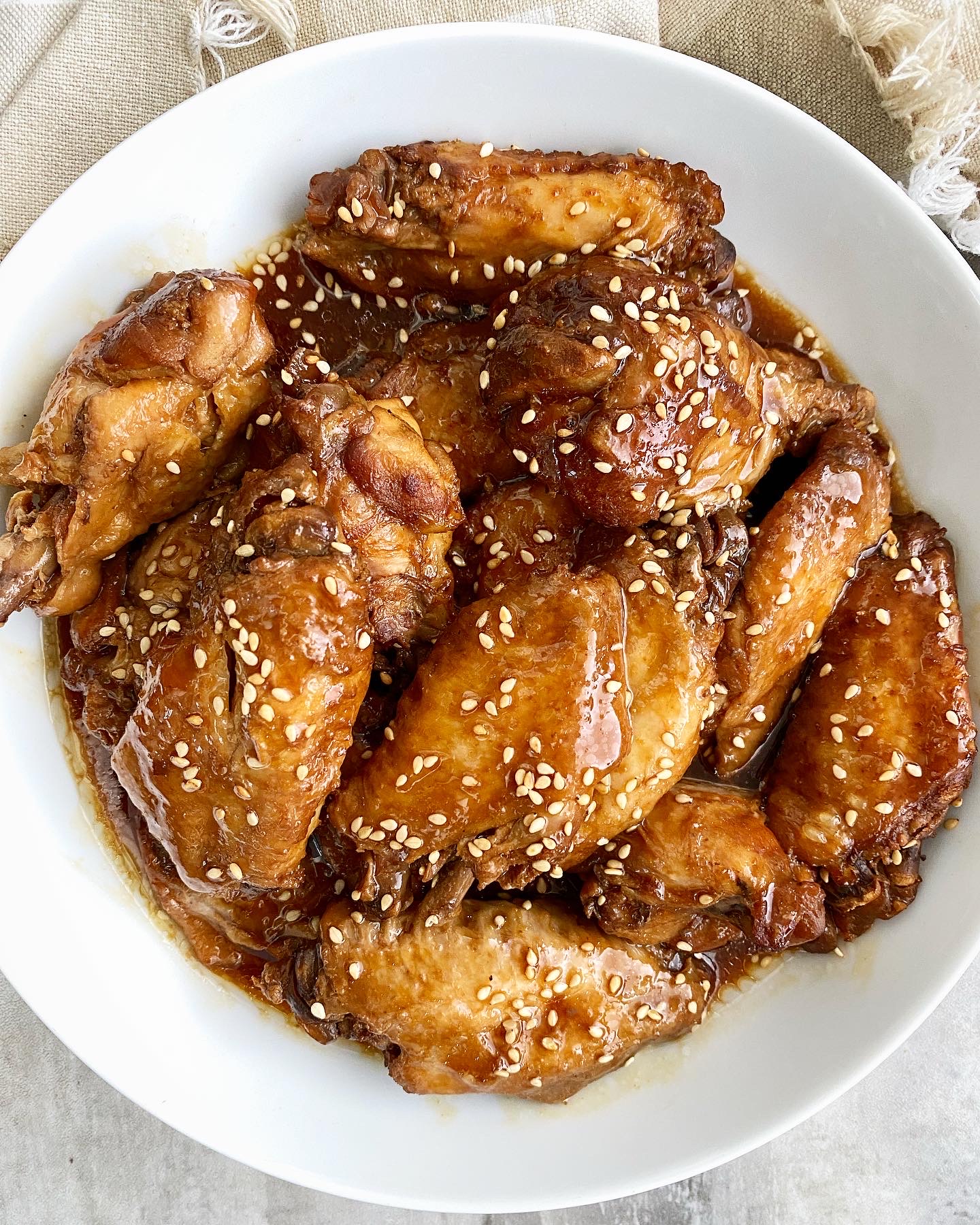 overhead shot of a pile of cooked teriyaki wings with sesame seeds garnish in a white bowl