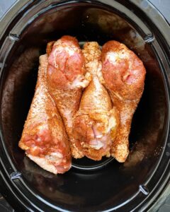 overhead shot of uncooked slow cooker turkey legs in a black slow cooker