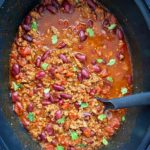 overhead shot of cooked beef chili in a black slow cooker garnished with fresh cilantro